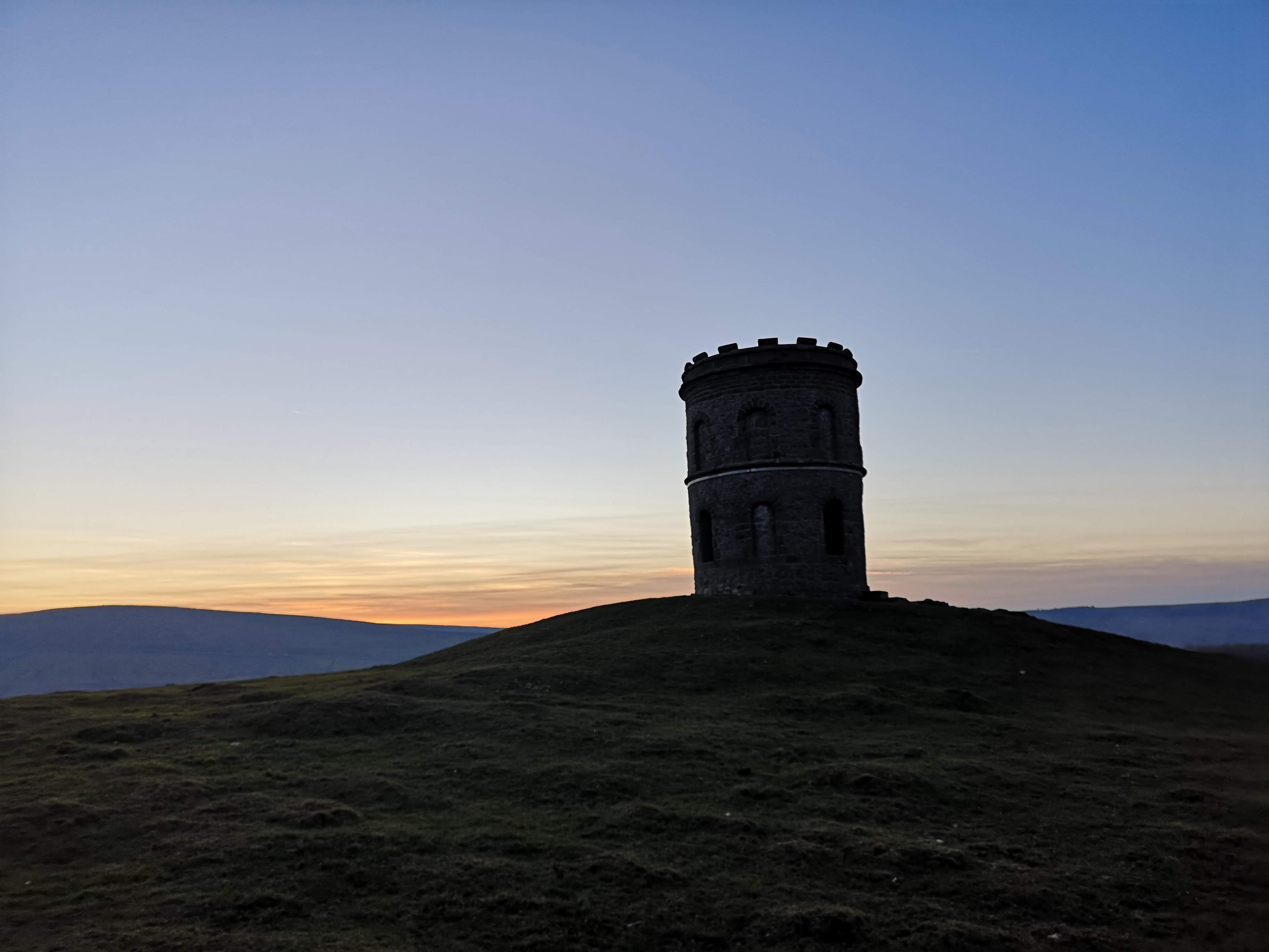 Stone tower monument silhouetted against sunset on Lake District summit