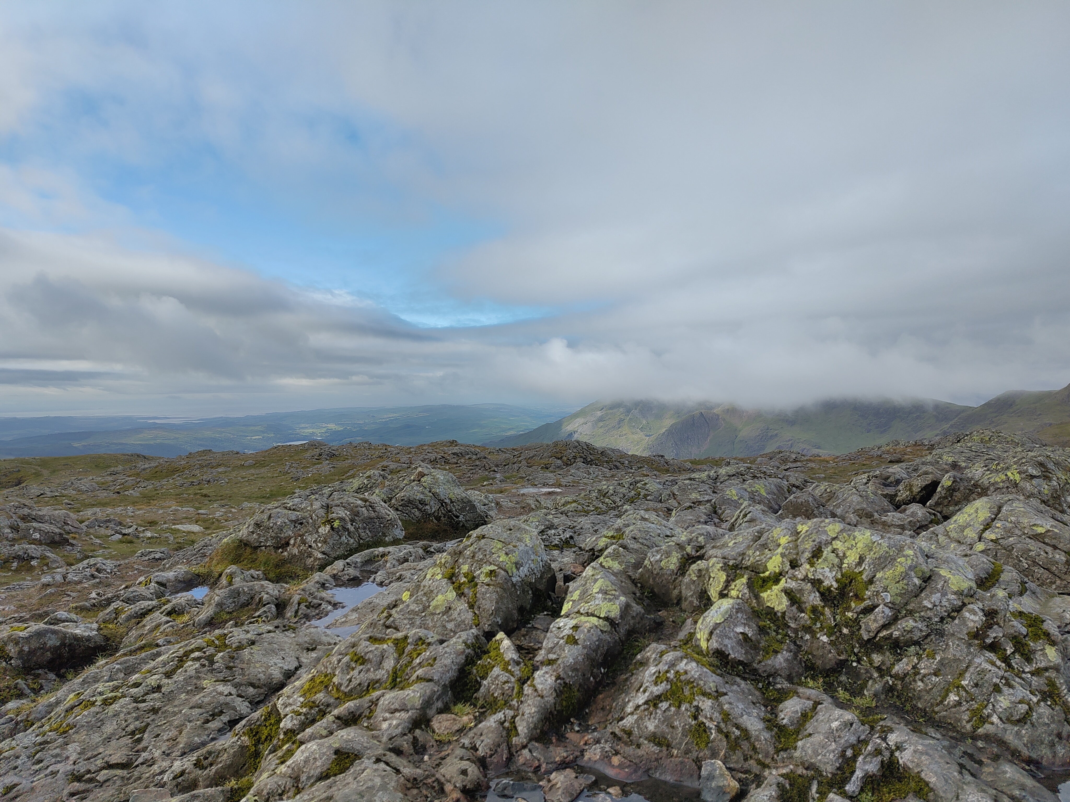 Moss-covered rocky mountain terrain with cloud-wrapped peaks in distance