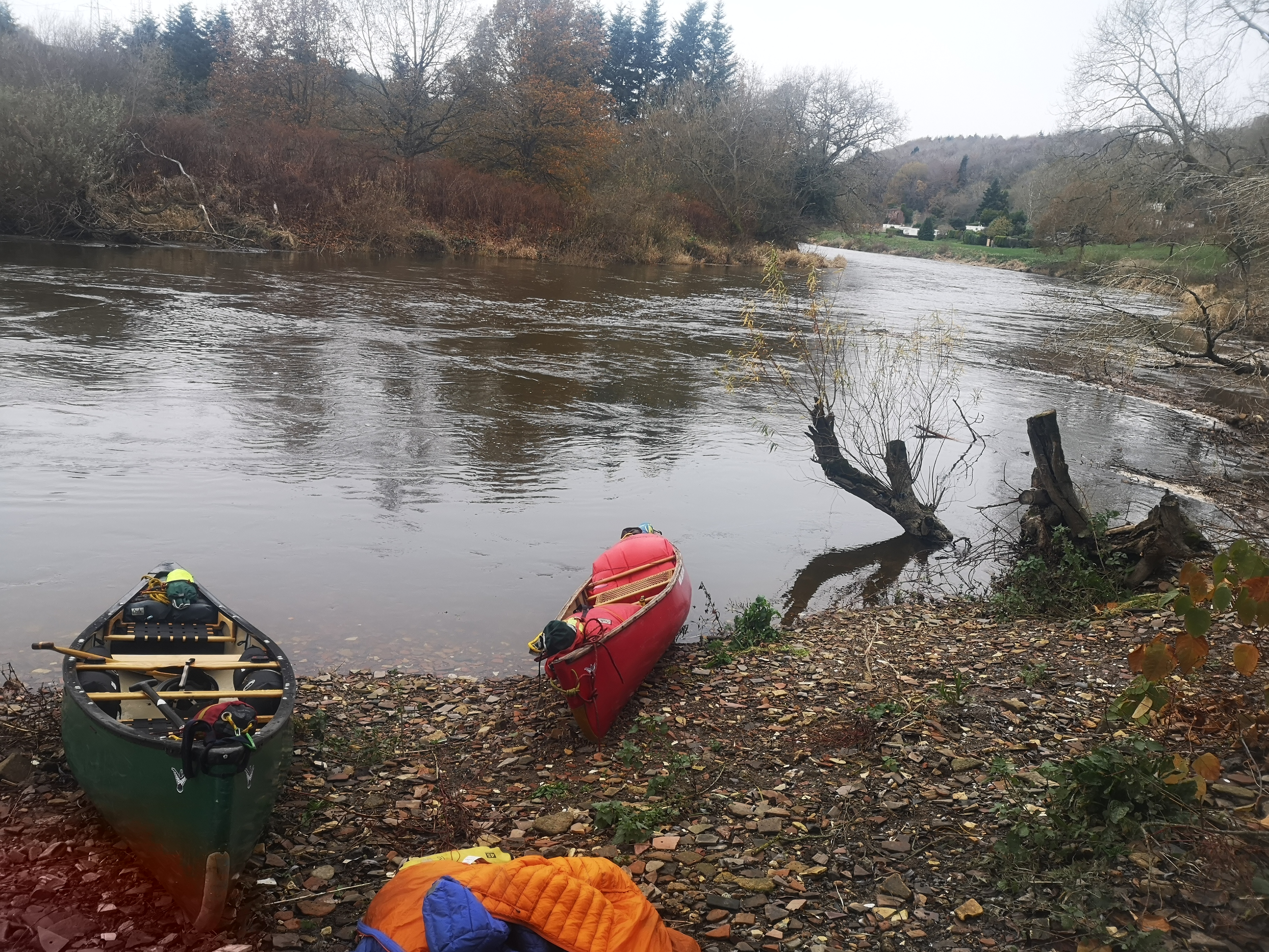 Two canoes and camping gear on riverbank during autumn expedition