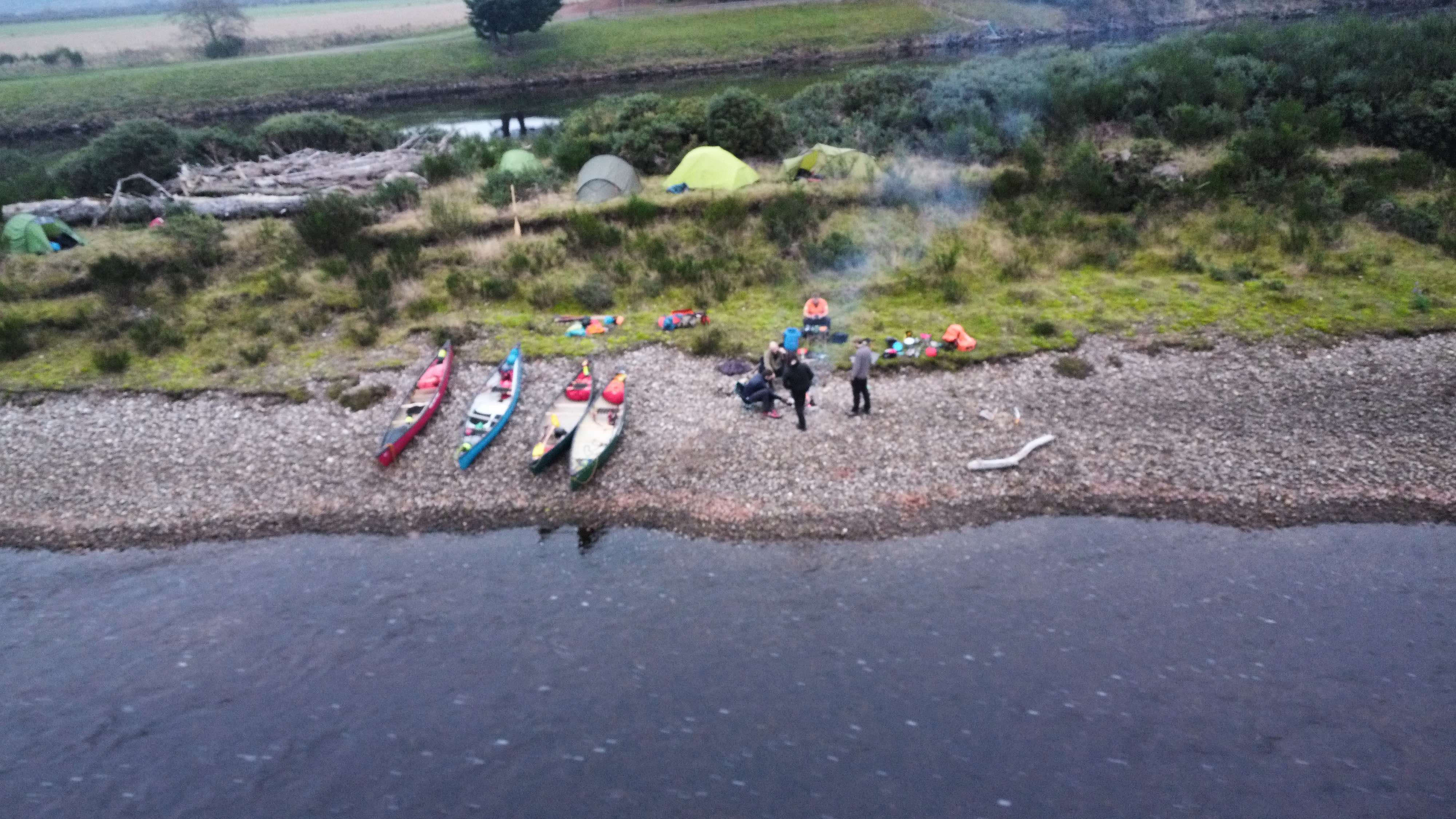 Aerial view of group expedition camp with canoes and tents by river