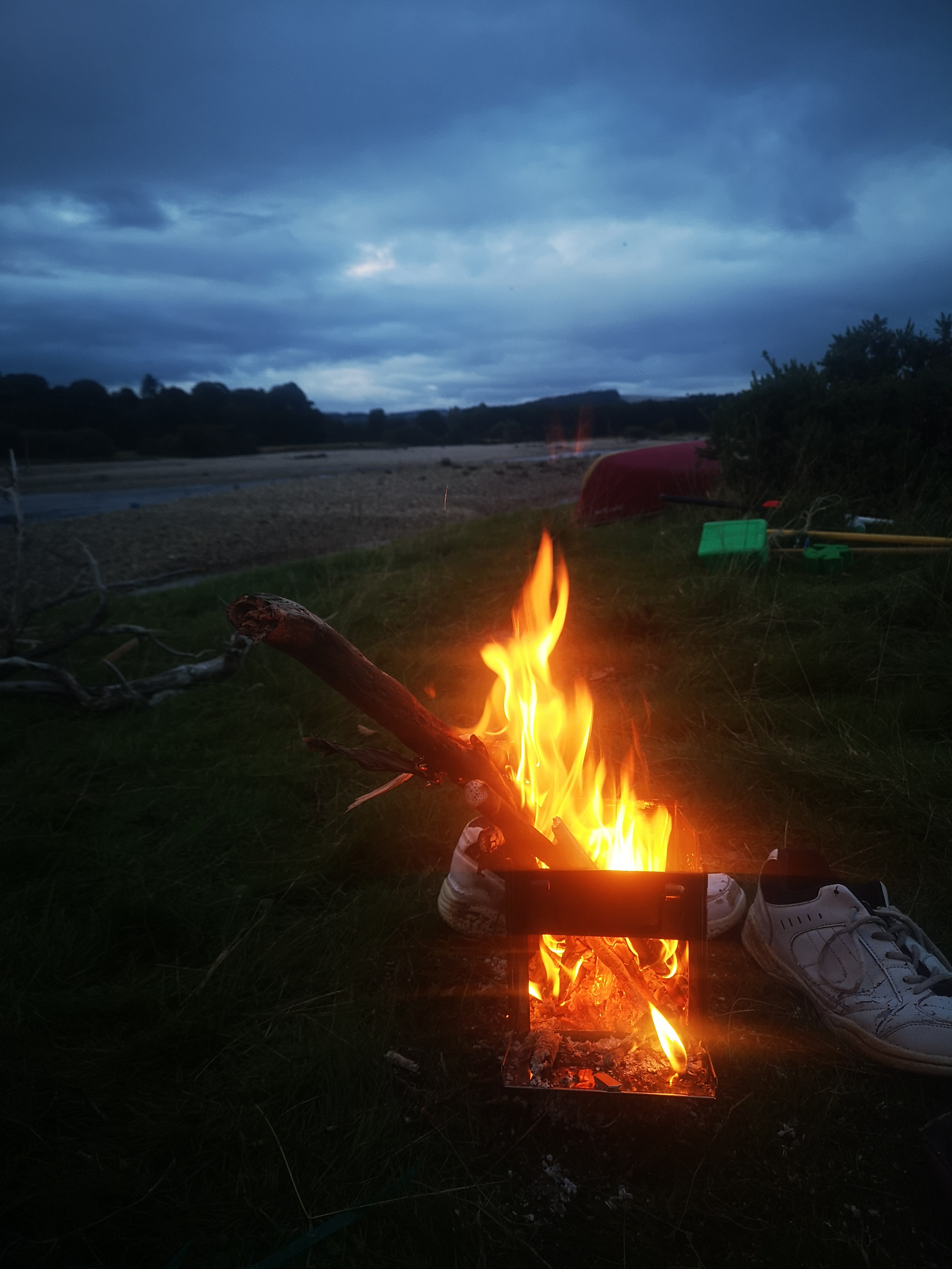 Glowing campfire at riverside campsite with canoes at dusk