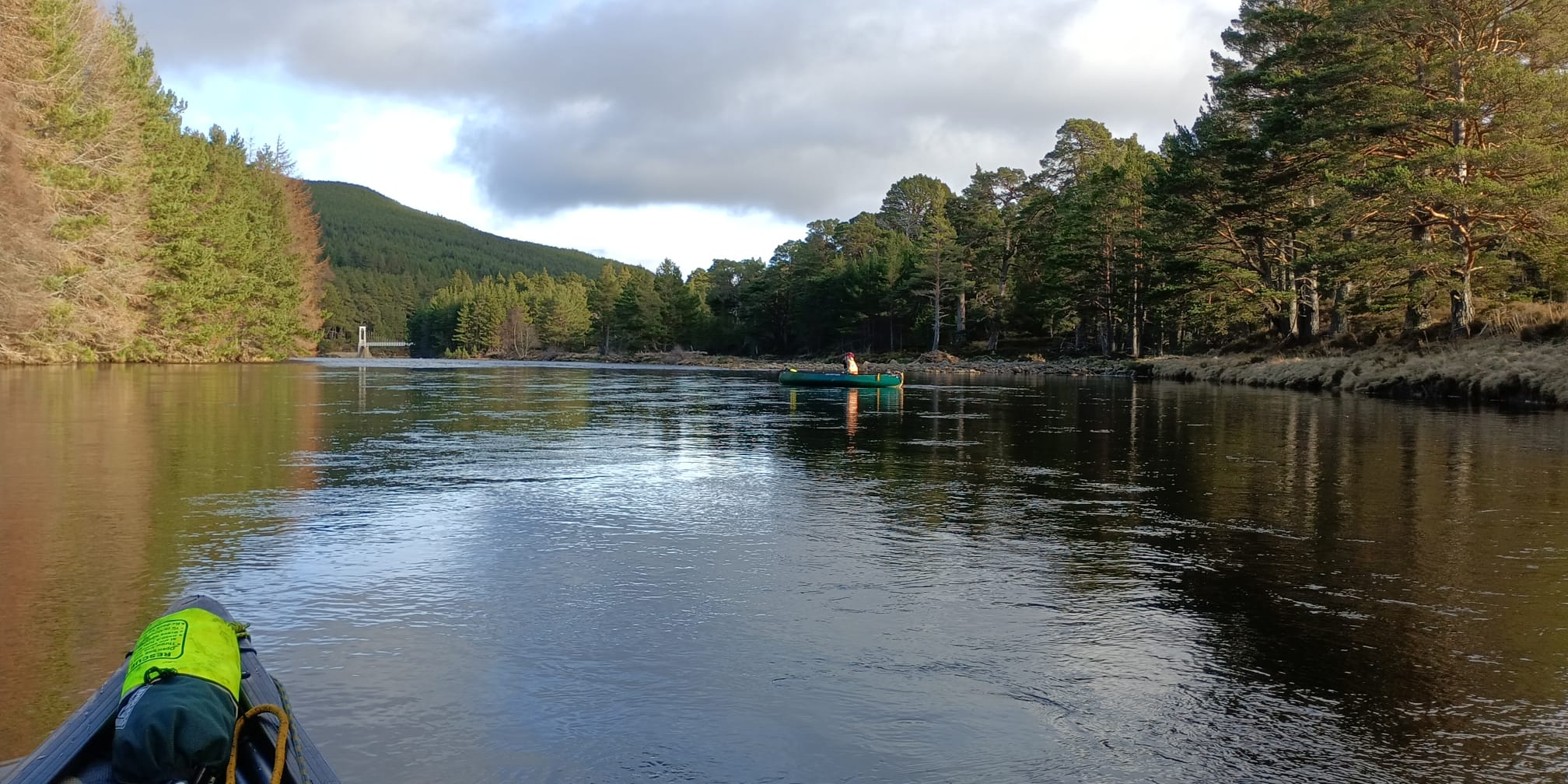 Canoe paddling on calm Scottish loch surrounded by forested mountains
