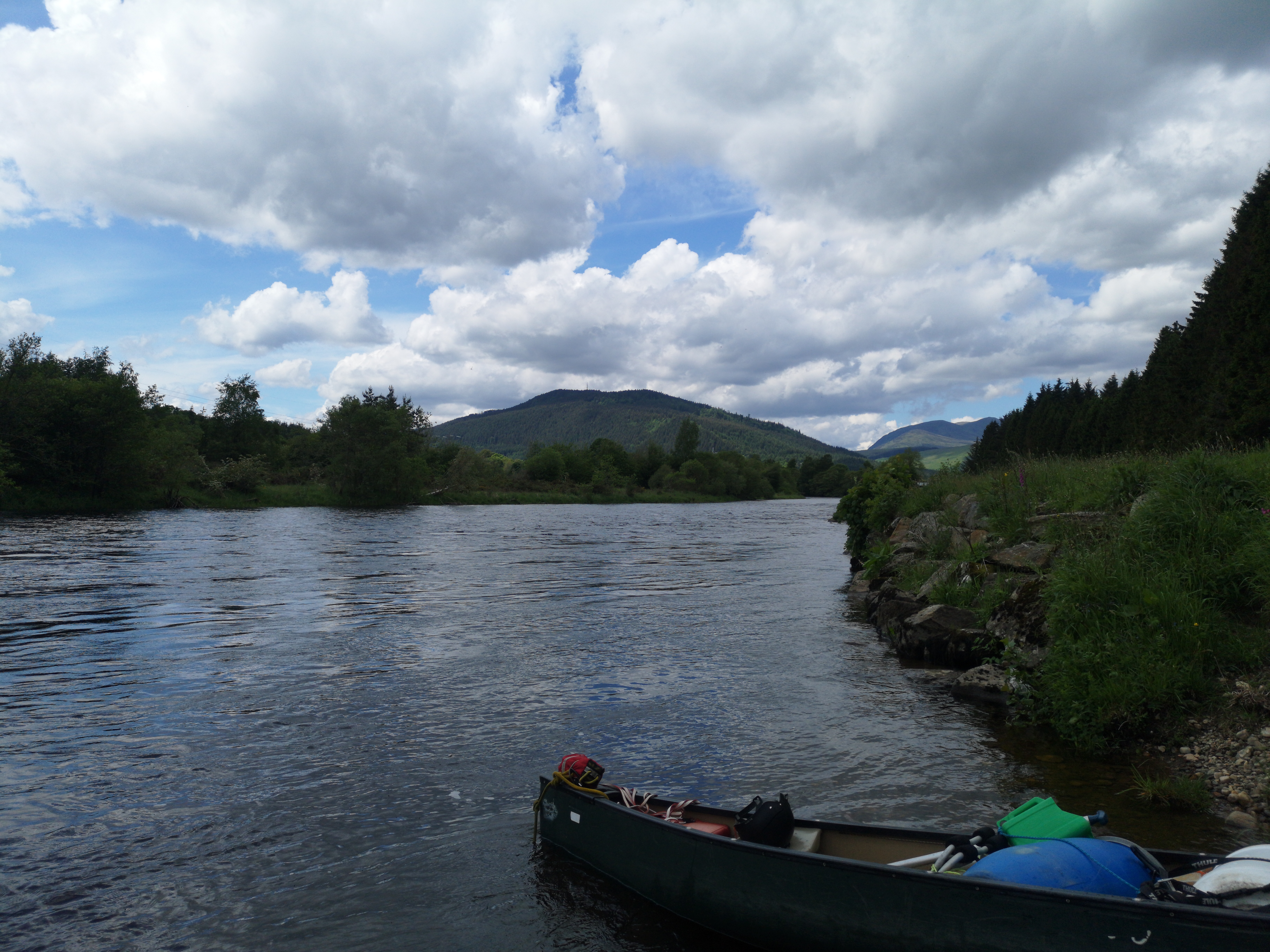 Green canoe resting on Scottish riverbank with mountains in background