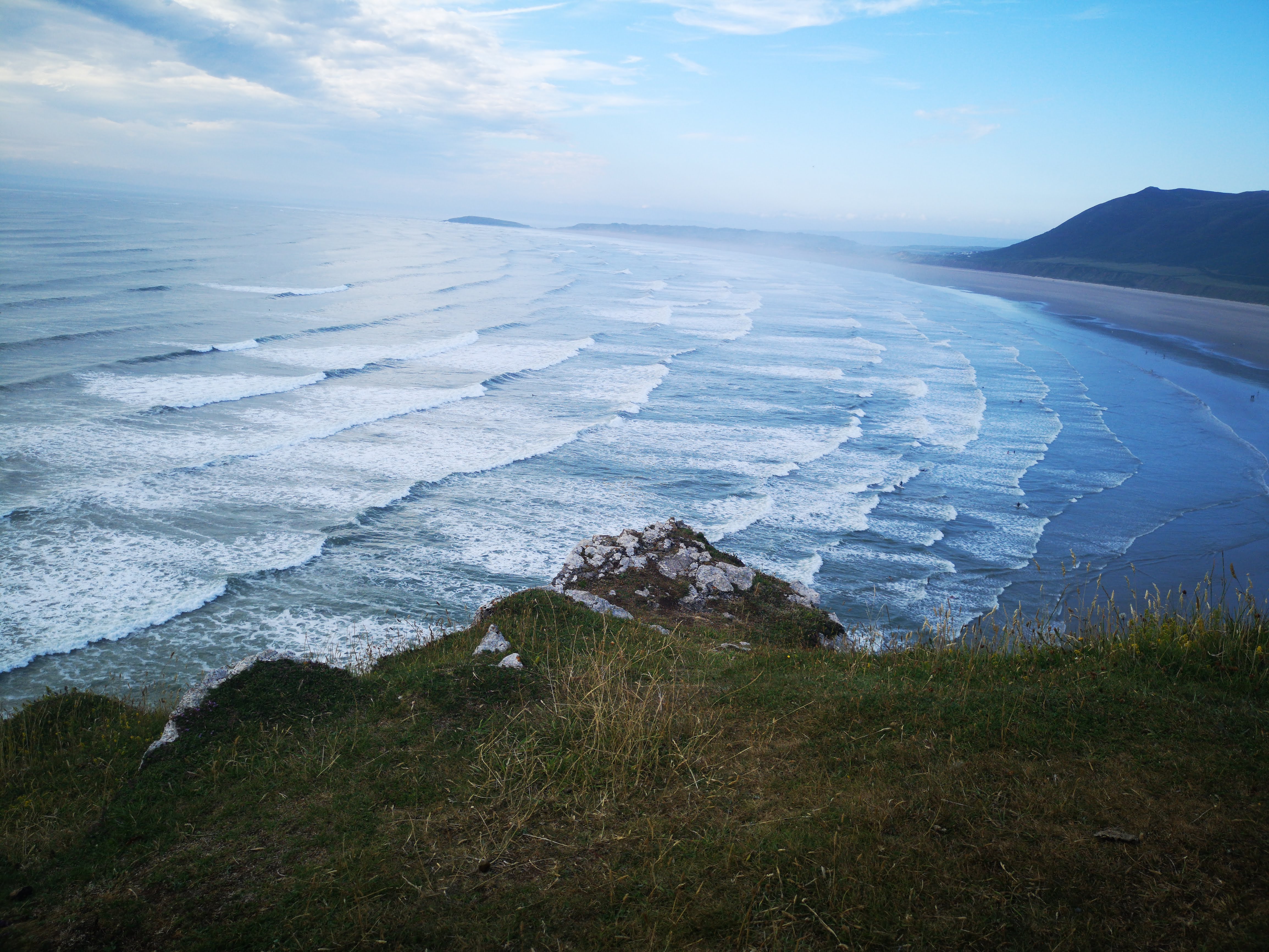Perfect waves breaking along long sandy beach viewed from coastal clifftop