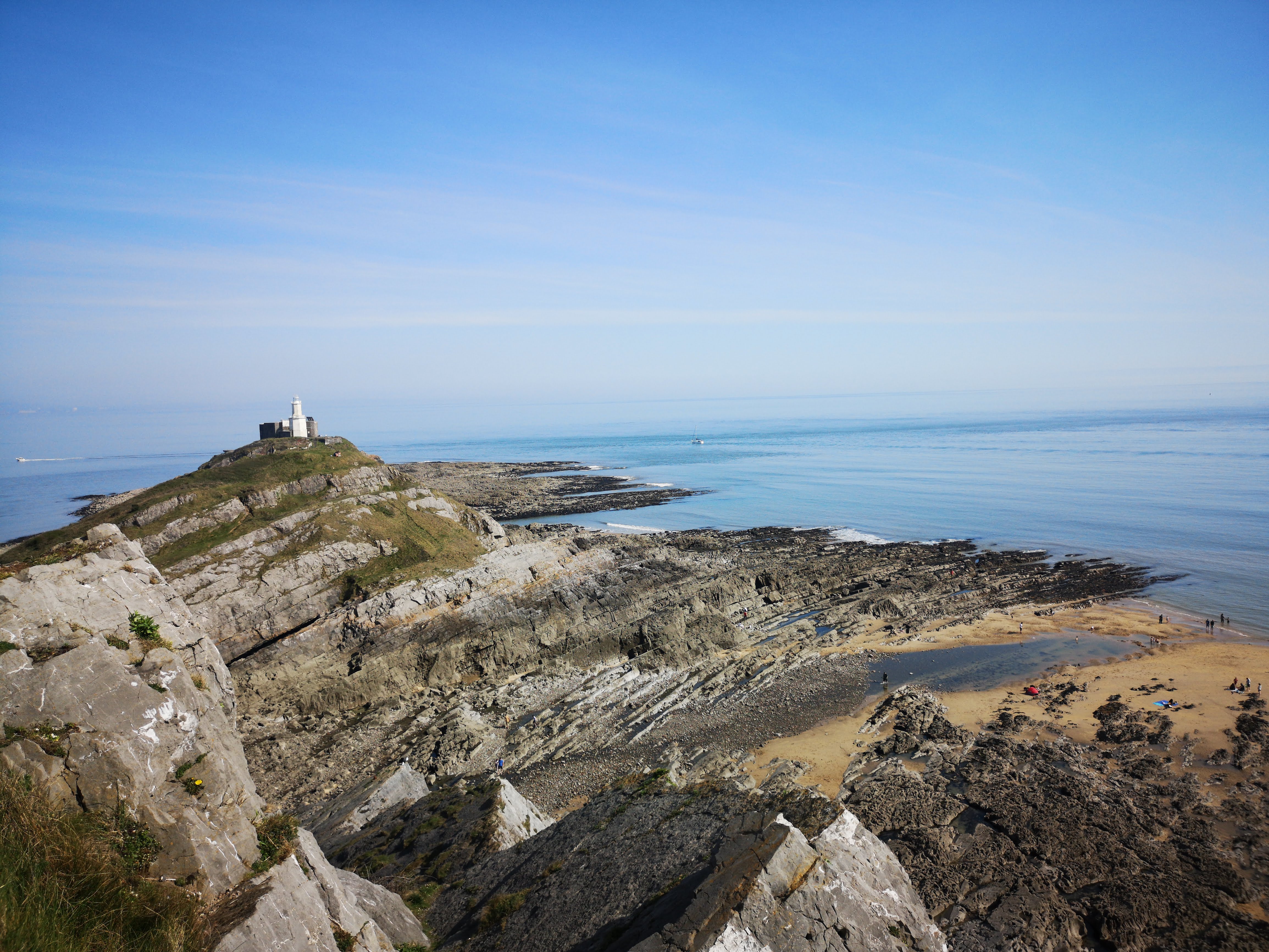 White lighthouse on dramatic rocky headland with beach below