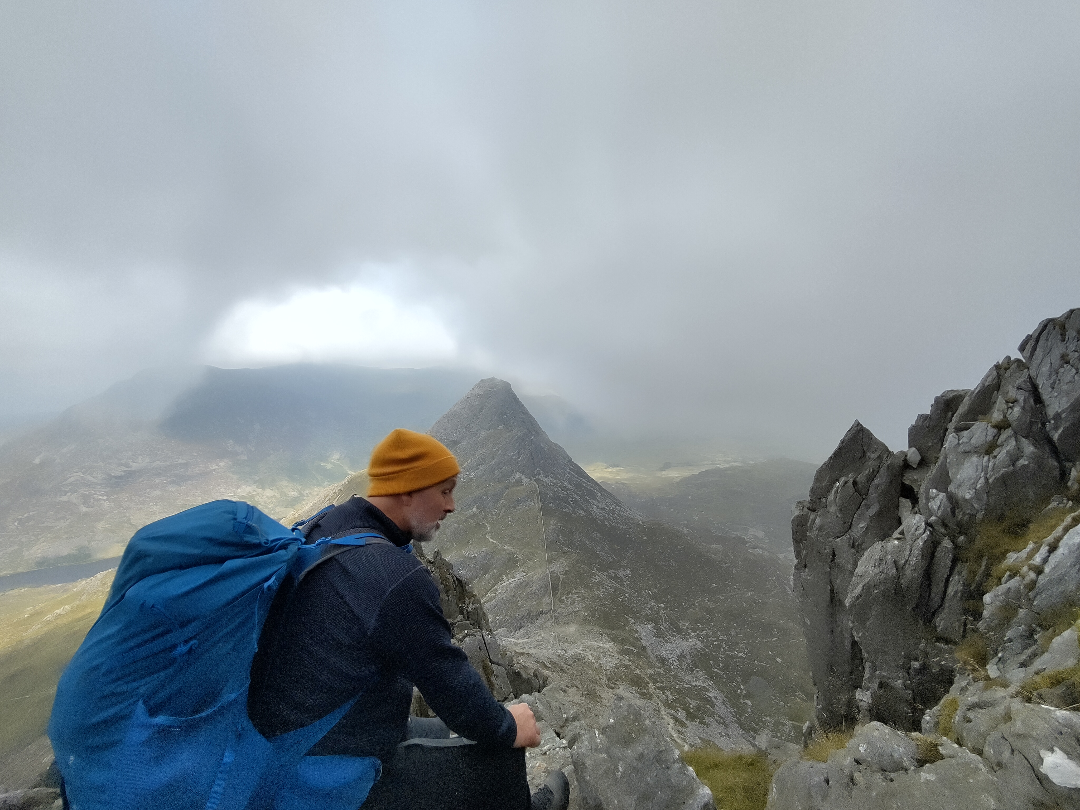 Hiker on dramatic misty mountain ridge with peak emerging from clouds