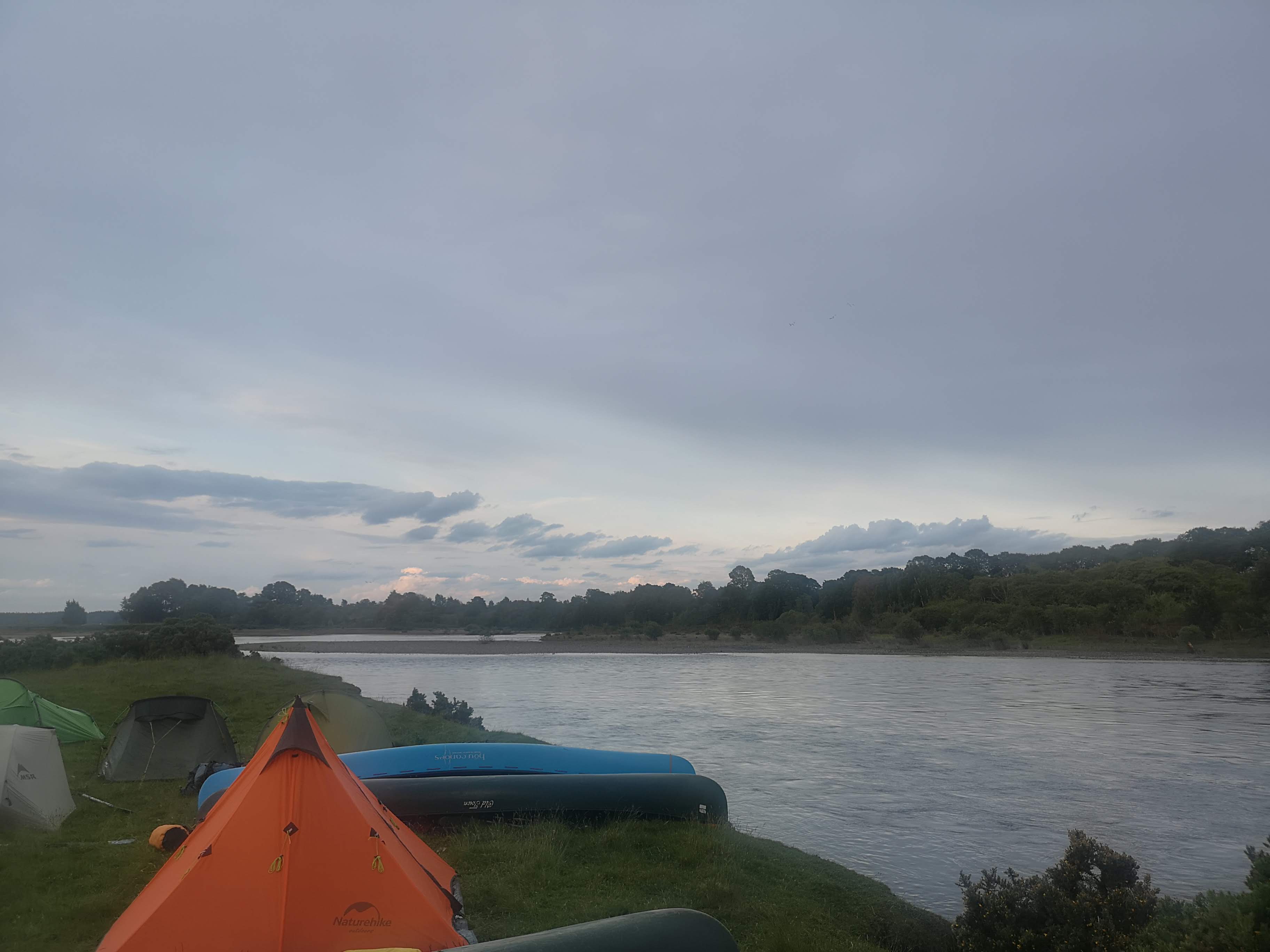 Evening camp with tents and canoes beside Scottish river