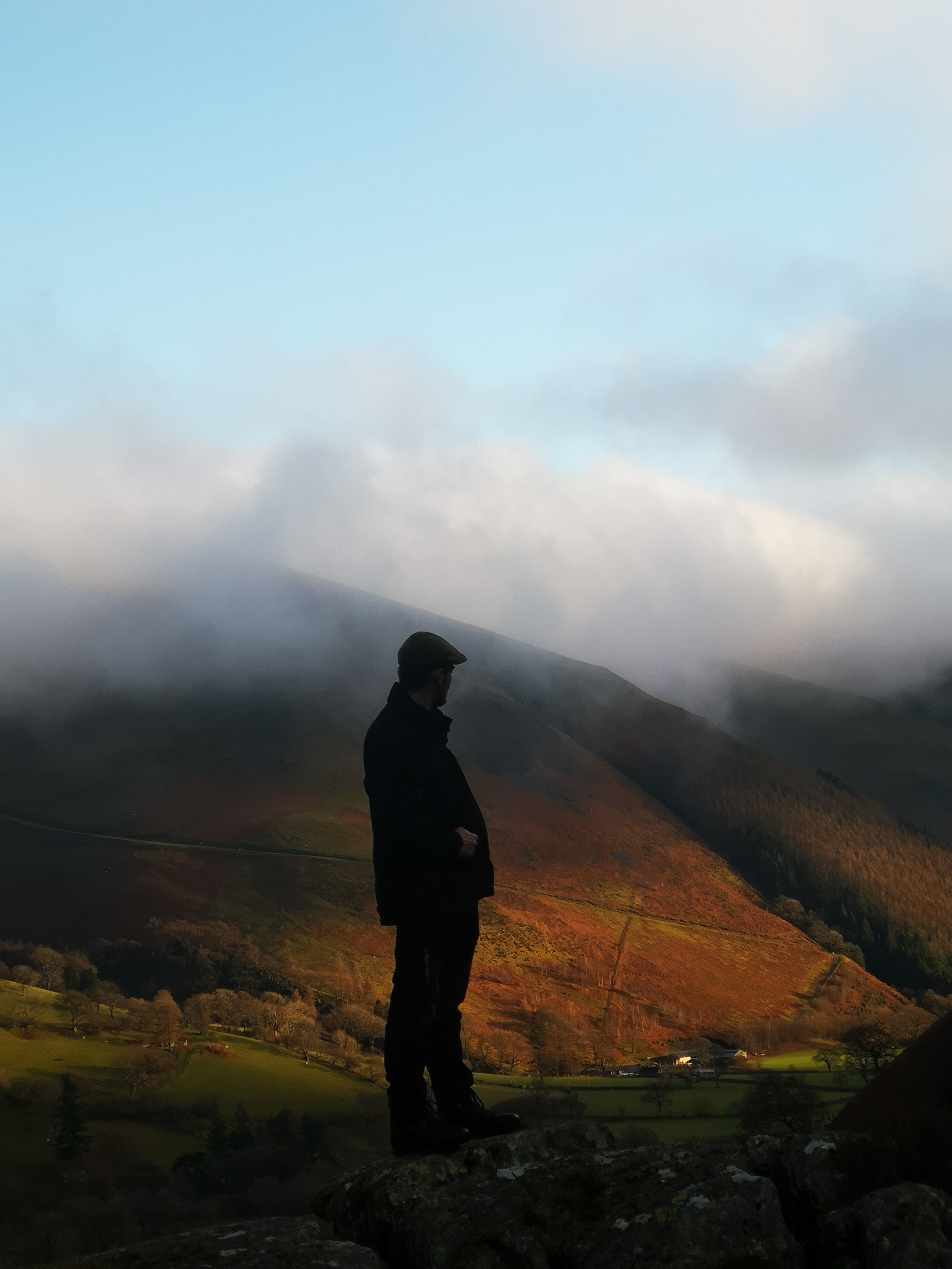 Silhouetted hiker overlooking misty autumn valley with dramatic light