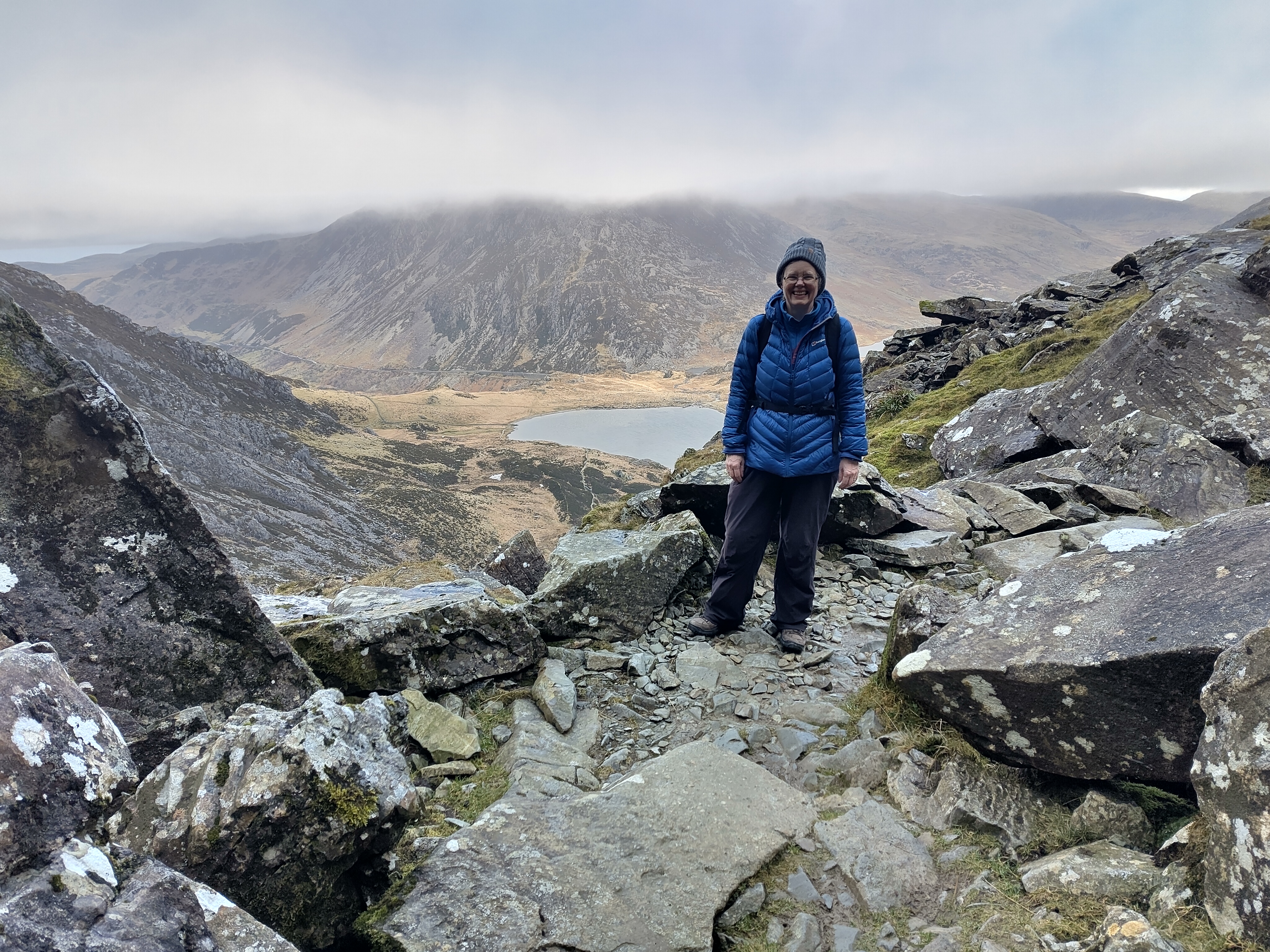 Hiker celebrating on rocky summit overlooking mountain tarn and valleys